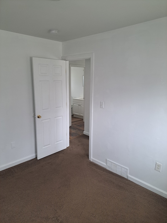 empty room featuring visible vents, baseboards, and dark colored carpet
