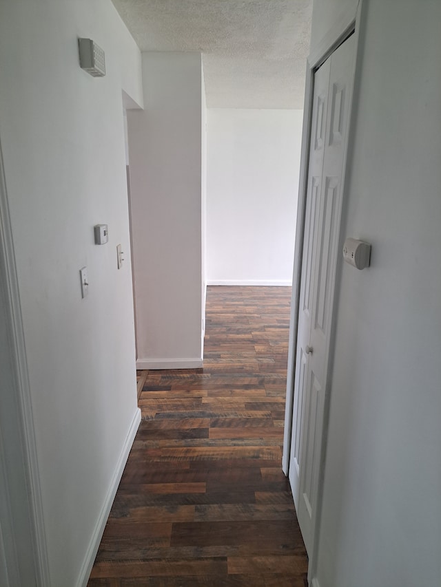 hall with a textured ceiling, baseboards, and wood finished floors