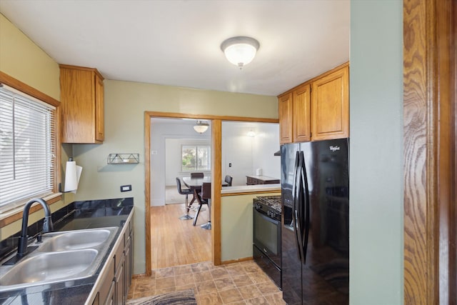kitchen with a sink, brown cabinets, black appliances, and dark countertops