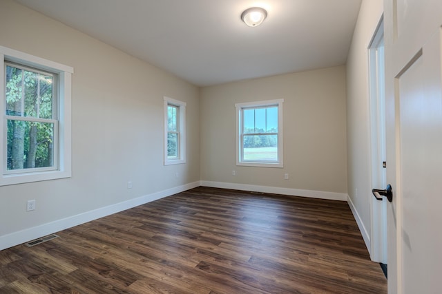 empty room featuring visible vents, baseboards, and dark wood-style flooring