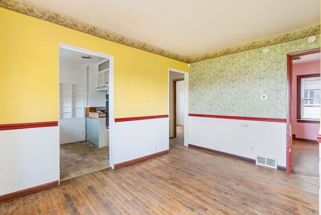 unfurnished room with a wainscoted wall, baseboards, wallpapered walls, wood finished floors, and visible vents