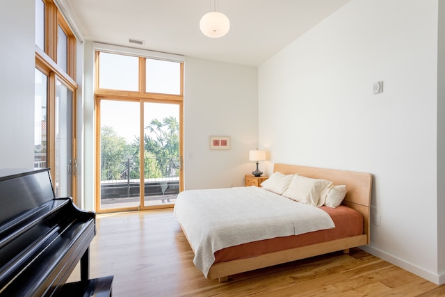 bedroom featuring a wall of windows, light wood-type flooring, visible vents, and access to outside