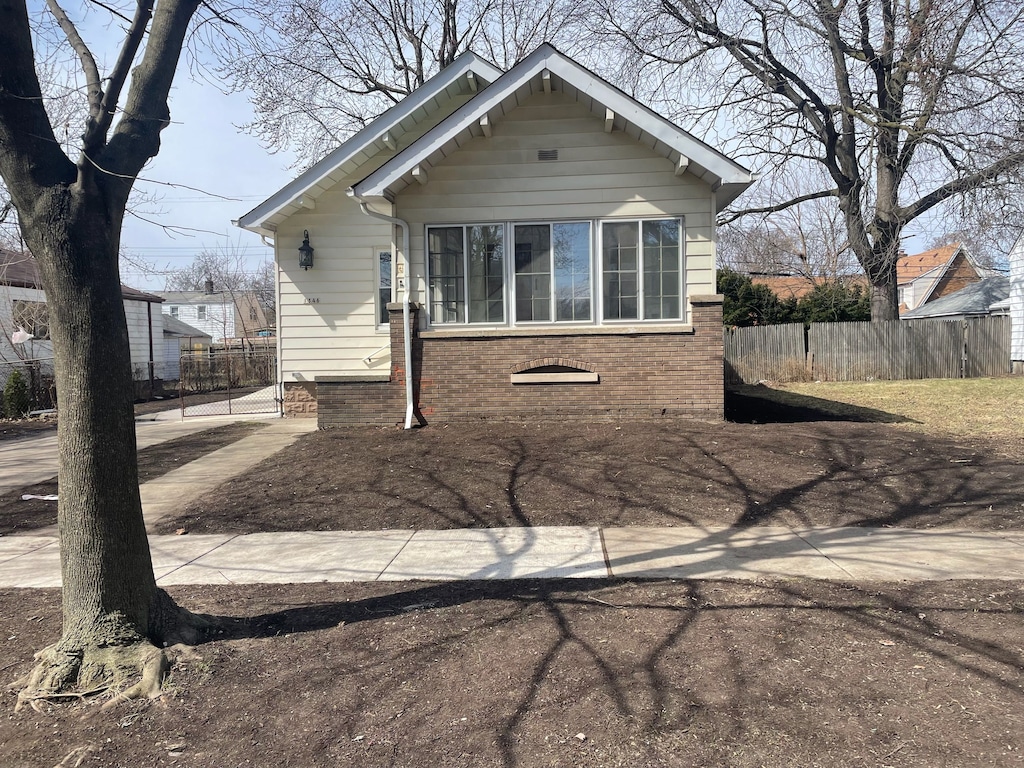 bungalow-style home featuring brick siding and fence
