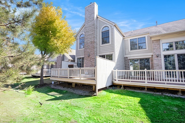 rear view of house featuring a deck, a lawn, and a chimney