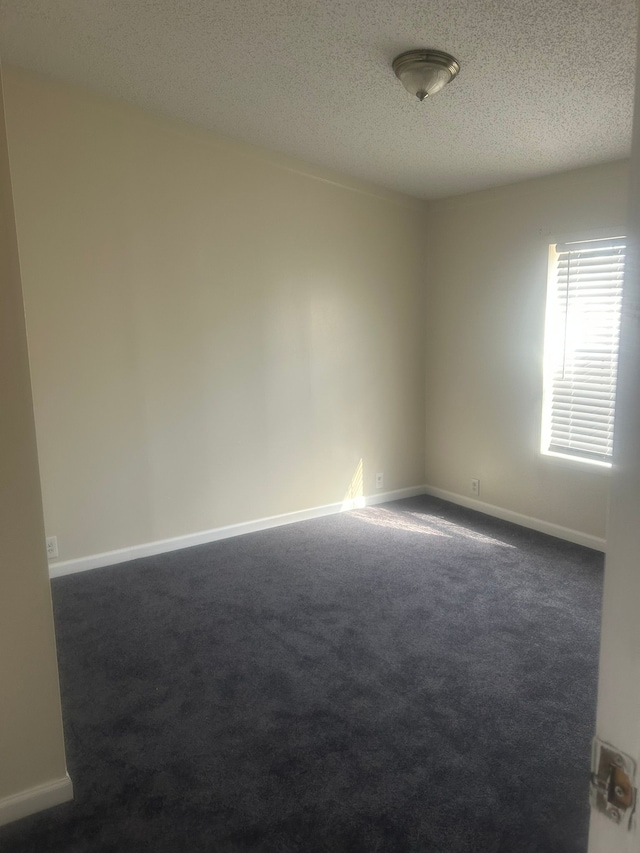 unfurnished room featuring baseboards, dark colored carpet, and a textured ceiling