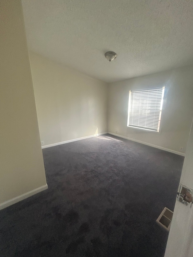 empty room with baseboards, visible vents, dark carpet, and a textured ceiling