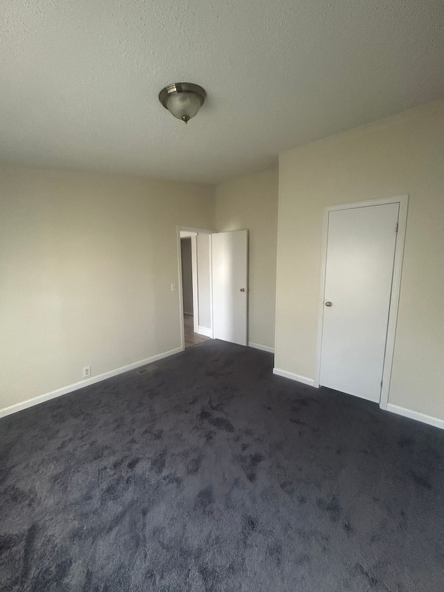 unfurnished room with baseboards, dark colored carpet, and a textured ceiling