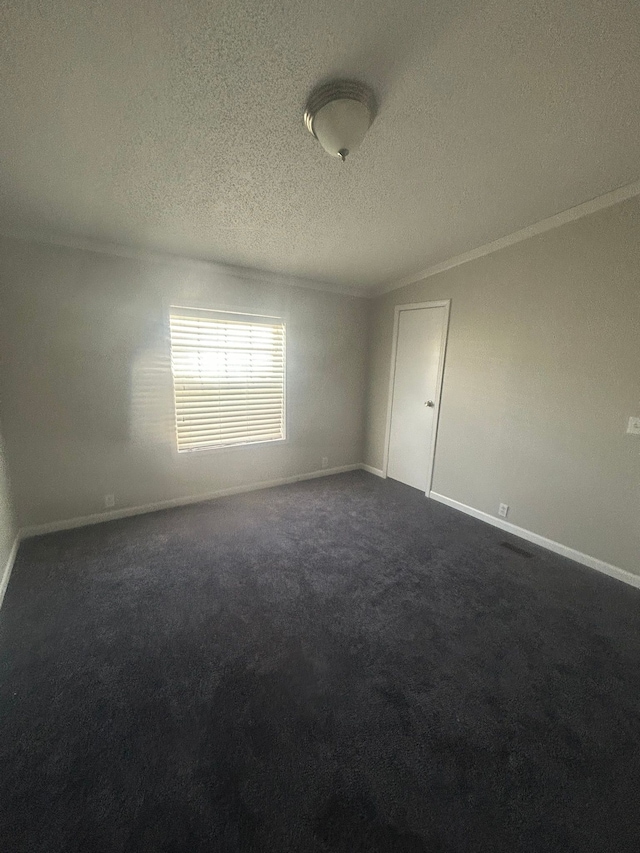 empty room featuring baseboards, dark colored carpet, ornamental molding, and a textured ceiling