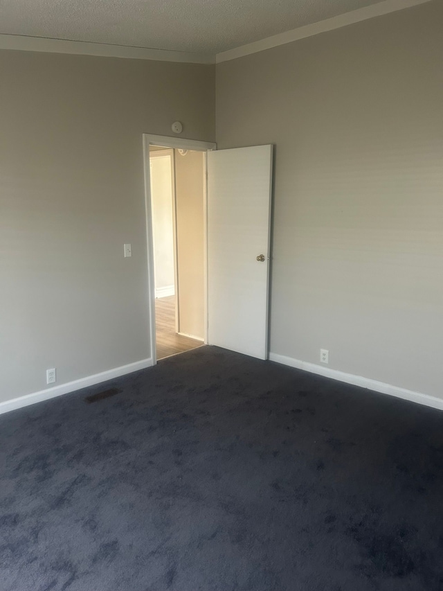 spare room with crown molding, a textured ceiling, dark colored carpet, baseboards, and visible vents