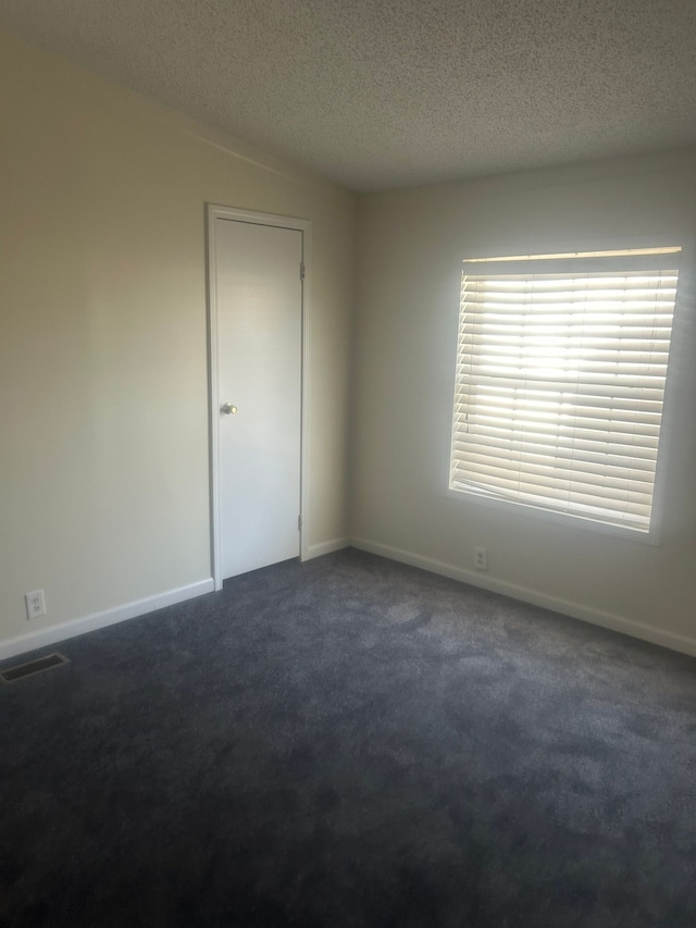 spare room with baseboards, a textured ceiling, dark colored carpet, and visible vents