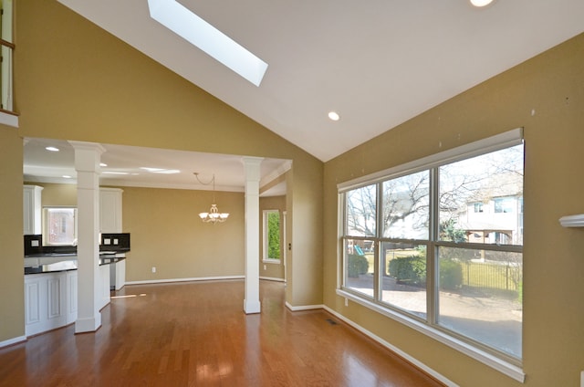 unfurnished living room featuring ornate columns, high vaulted ceiling, dark wood-type flooring, baseboards, and a skylight
