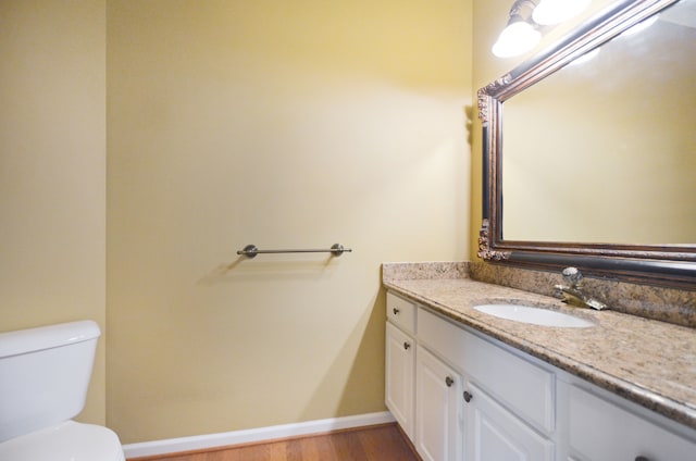 half bathroom with toilet, vanity, baseboards, and wood finished floors