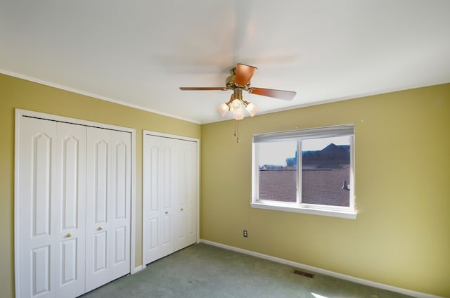 unfurnished bedroom with carpet flooring, baseboards, visible vents, two closets, and ceiling fan