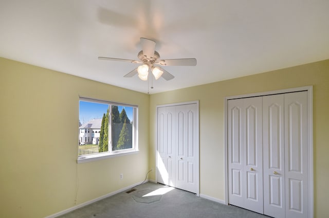 unfurnished bedroom with visible vents, carpet, two closets, baseboards, and a ceiling fan