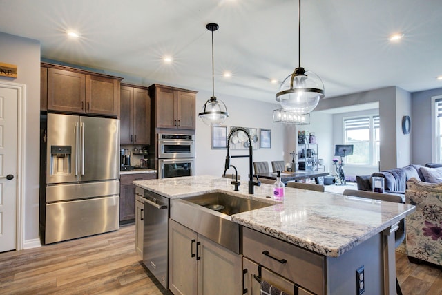kitchen featuring a sink, appliances with stainless steel finishes, light wood-style floors, open floor plan, and light stone countertops