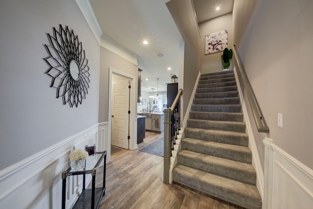 stairs with recessed lighting, wood finished floors, a decorative wall, a wainscoted wall, and crown molding