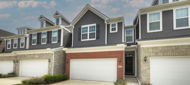 view of property with driveway, stone siding, a garage, and brick siding
