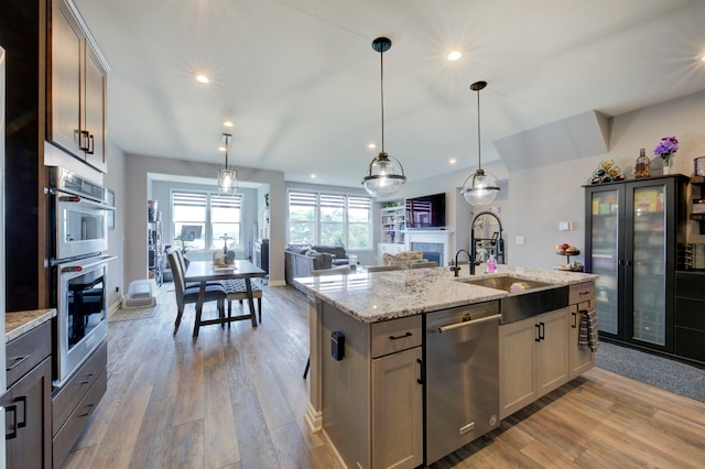 kitchen featuring recessed lighting, a sink, stainless steel appliances, a fireplace, and light wood-type flooring