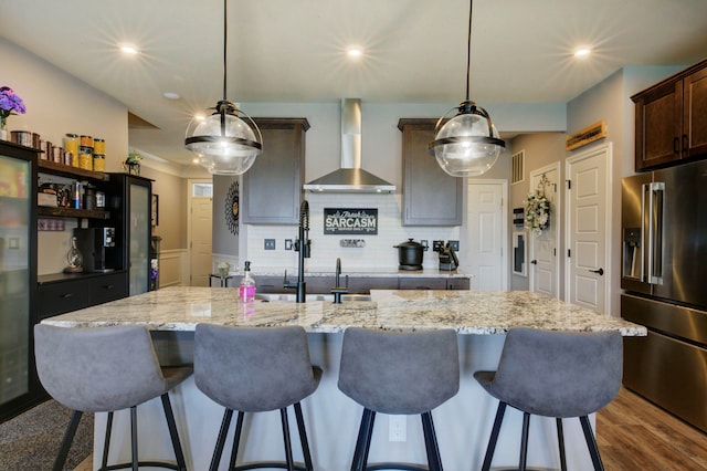 kitchen with high end refrigerator, tasteful backsplash, wall chimney exhaust hood, dark brown cabinetry, and visible vents