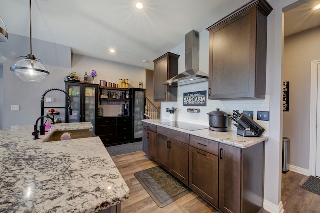 kitchen with a sink, tasteful backsplash, wall chimney exhaust hood, dark brown cabinetry, and wood finished floors
