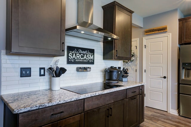 kitchen featuring black electric stovetop, wall chimney exhaust hood, dark brown cabinets, wood finished floors, and stainless steel fridge with ice dispenser