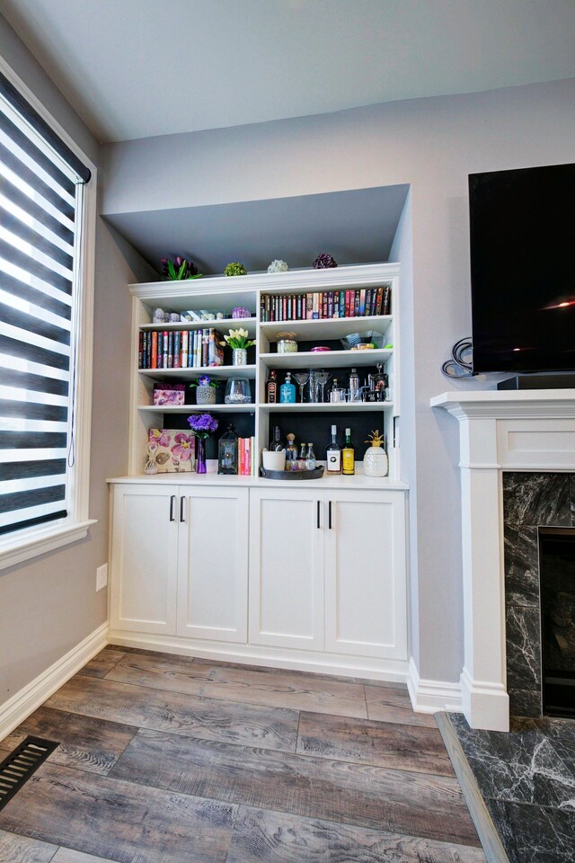 bar featuring baseboards, visible vents, a high end fireplace, and light wood finished floors