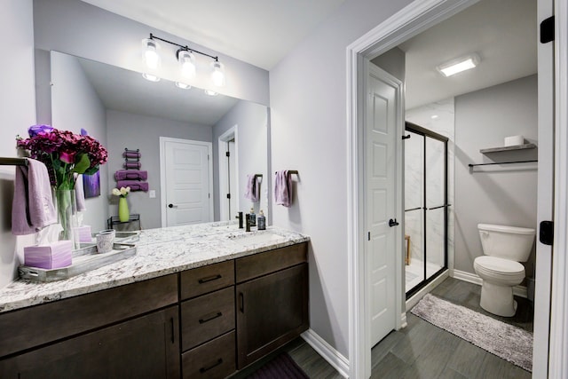 bathroom featuring vanity, toilet, a stall shower, baseboards, and wood finished floors