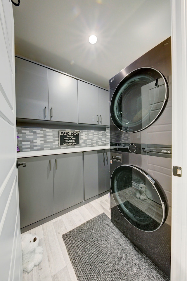 laundry area with light wood finished floors, recessed lighting, cabinet space, and stacked washer and clothes dryer