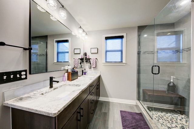 full bath with baseboards, a shower stall, double vanity, and a sink
