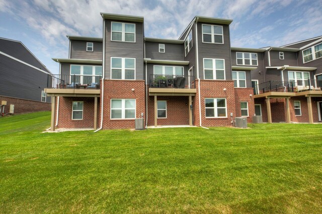 rear view of house featuring cooling unit, a lawn, and brick siding