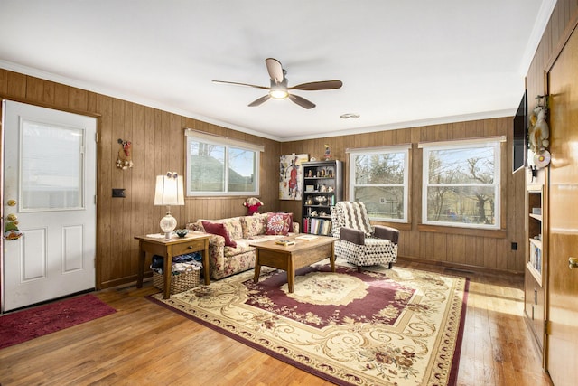 living area with wooden walls, ornamental molding, a ceiling fan, and hardwood / wood-style flooring