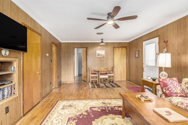 living area with light wood-style floors, ceiling fan, and crown molding