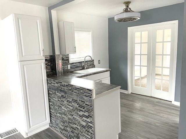 kitchen featuring french doors, white cabinetry, decorative backsplash, a sink, and wood finished floors