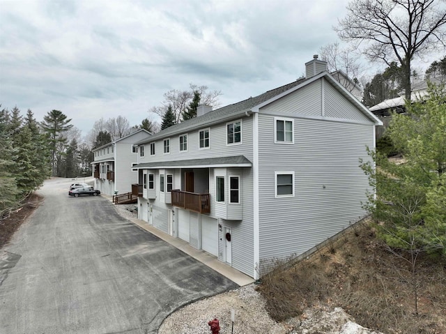 exterior space featuring aphalt driveway, an attached garage, a chimney, and a shingled roof