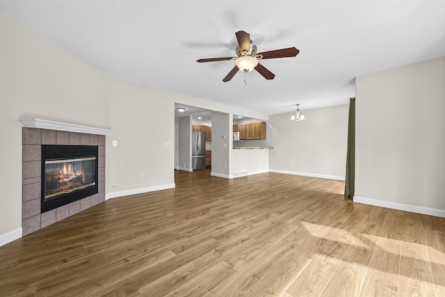 unfurnished living room featuring wood finished floors, a ceiling fan, visible vents, baseboards, and a fireplace