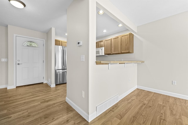 kitchen with white microwave, visible vents, freestanding refrigerator, and light wood-style floors