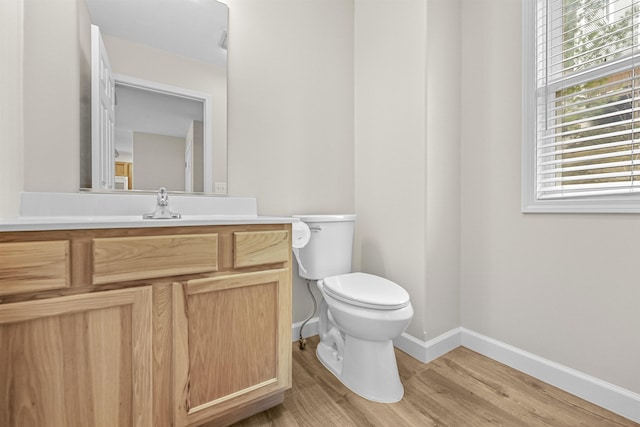 half bathroom with toilet, vanity, baseboards, and wood finished floors