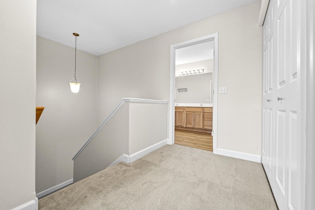 corridor with an upstairs landing, baseboards, and light carpet