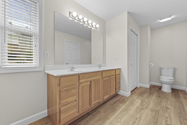 full bath featuring toilet, a sink, wood finished floors, double vanity, and baseboards