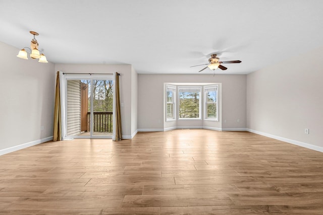 interior space featuring wood finished floors, ceiling fan with notable chandelier, and baseboards