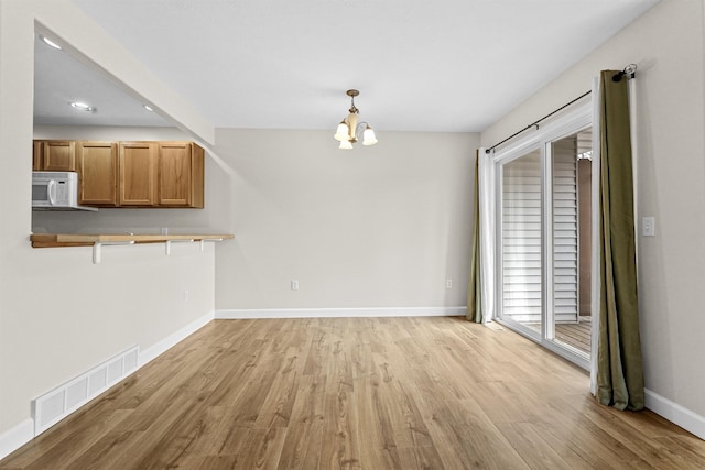 unfurnished dining area featuring a notable chandelier, baseboards, visible vents, and light wood finished floors