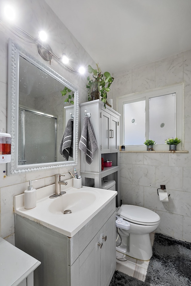 bathroom with a shower stall, toilet, vanity, marble finish floor, and tile walls