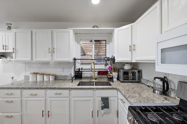 kitchen with white cabinetry, white microwave, stainless steel gas range, and a sink