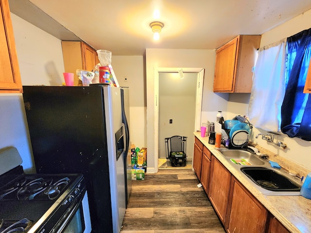 kitchen with light countertops, dark wood-style flooring, gas range oven, a sink, and brown cabinetry