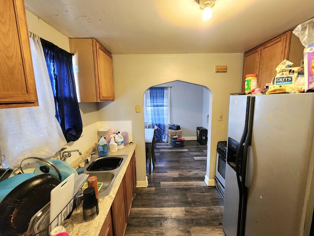 kitchen with stove, dark wood-style flooring, a sink, freestanding refrigerator, and brown cabinets