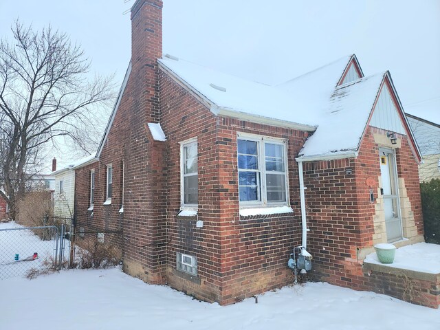 view of snow covered exterior featuring brick siding, fence, and a chimney
