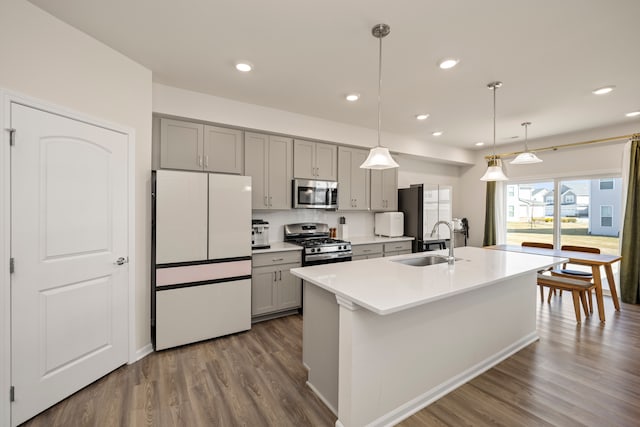kitchen featuring gray cabinets, dark wood-style flooring, a sink, a kitchen island with sink, and appliances with stainless steel finishes