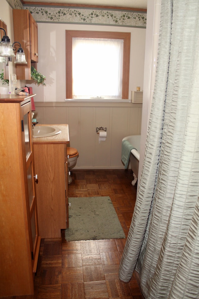 bathroom with a decorative wall, toilet, vanity, and a wainscoted wall