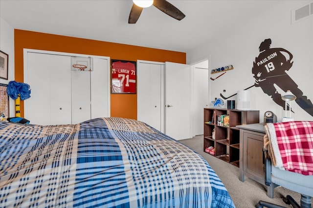 bedroom featuring visible vents, carpet flooring, a ceiling fan, and multiple closets
