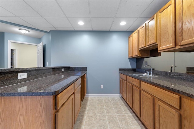 kitchen with a sink, a drop ceiling, dark stone countertops, recessed lighting, and baseboards